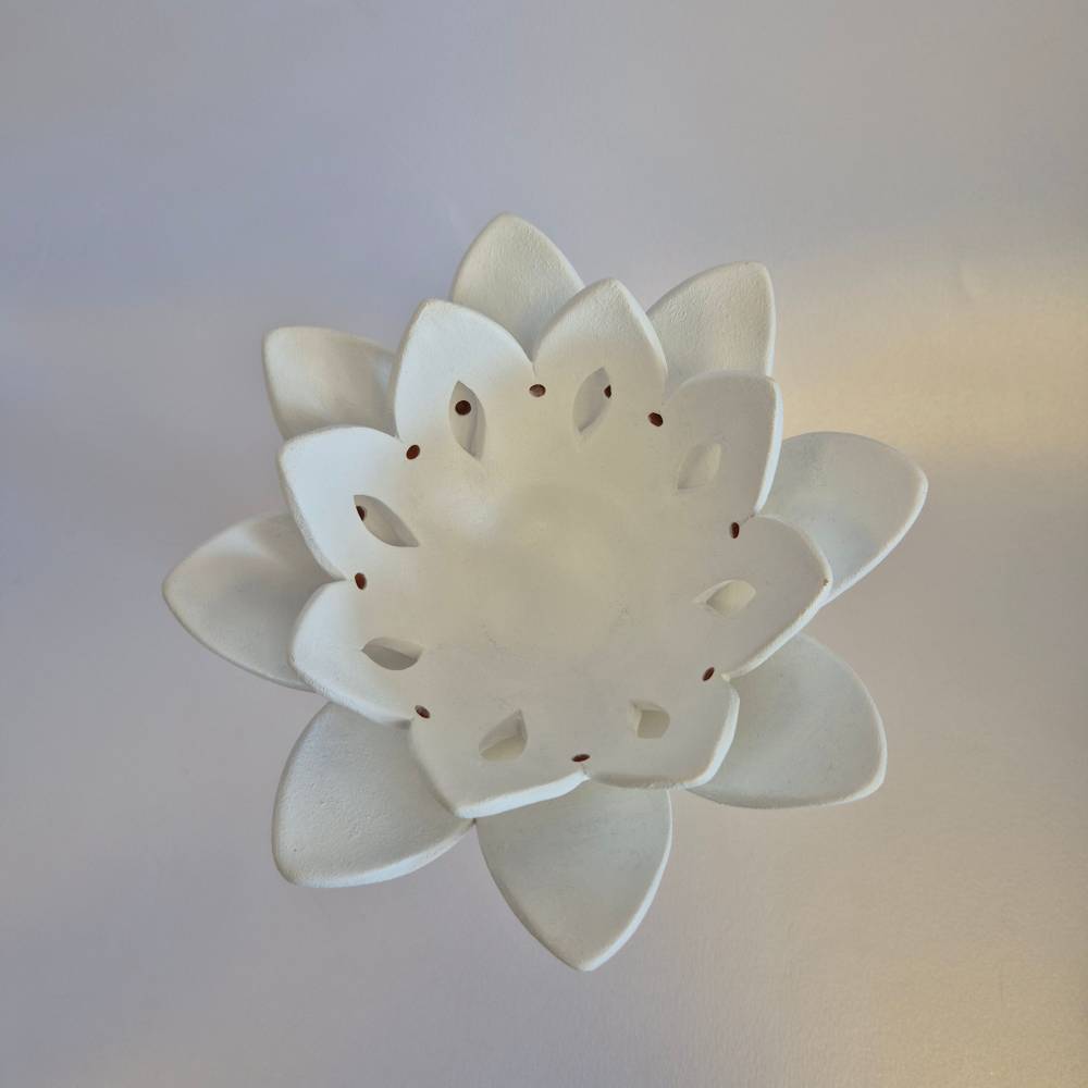Seimos-zidinys-zvakide_Keramikinis-lotoso-ziedas-ant-kojeles_5_salonassandrijlt_ White ceramic lotus flower with perforated petals, a decorative decorative ornament/candle holder edge.