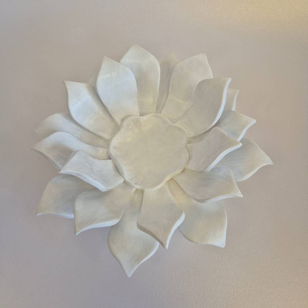 Seimos-zidinys-zvakide_Keramikinis-lotoso-ziedas-ant-kojeles_7_salonassandrijlt_ White ceramic flower wall sculpture with layered petals mounted on a pale wall