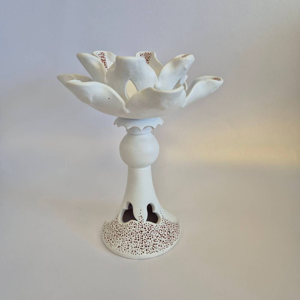 Seimos-zidinys-zvakide_Keramikinis-lotoso-ziedas-ant-kojeles_8_salonassandrijlt_ White ceramic sculpture of a stylized lotus flower on a pedestal with a perforated, lacy base.